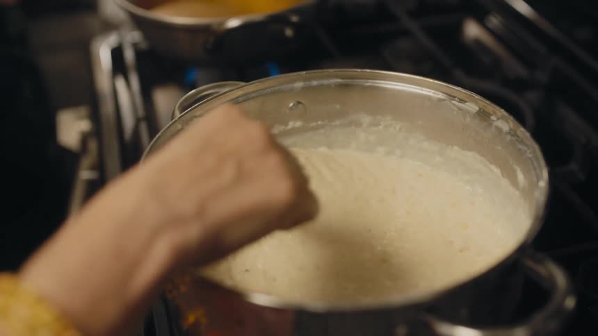 Woman stirs pot of food sitting on gas burning stove top