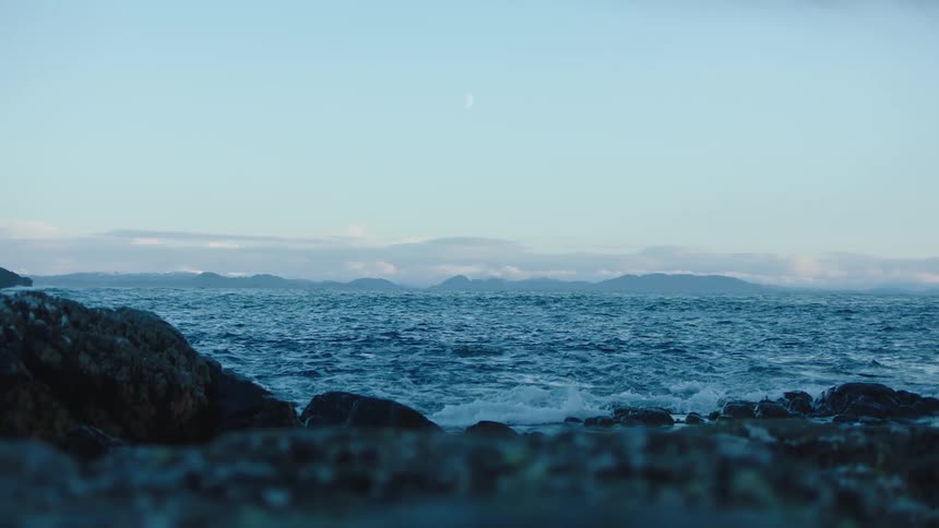 Rocks on the shore as waves roll in with hills in the distance