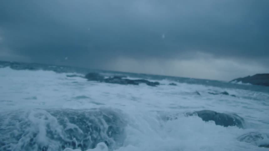 An ocean wave crashing ashore with storm clouds in the distance