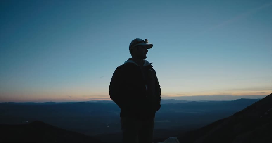 A silhouetted man standing in mountains with a headlamp