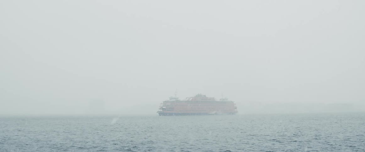 The orange staten island ferry in the fog and snow
