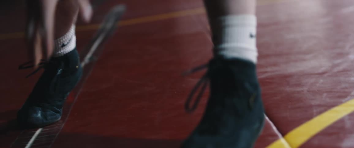 A wrestler takes a stance and moves around a wrestling circle on gym padded floor
