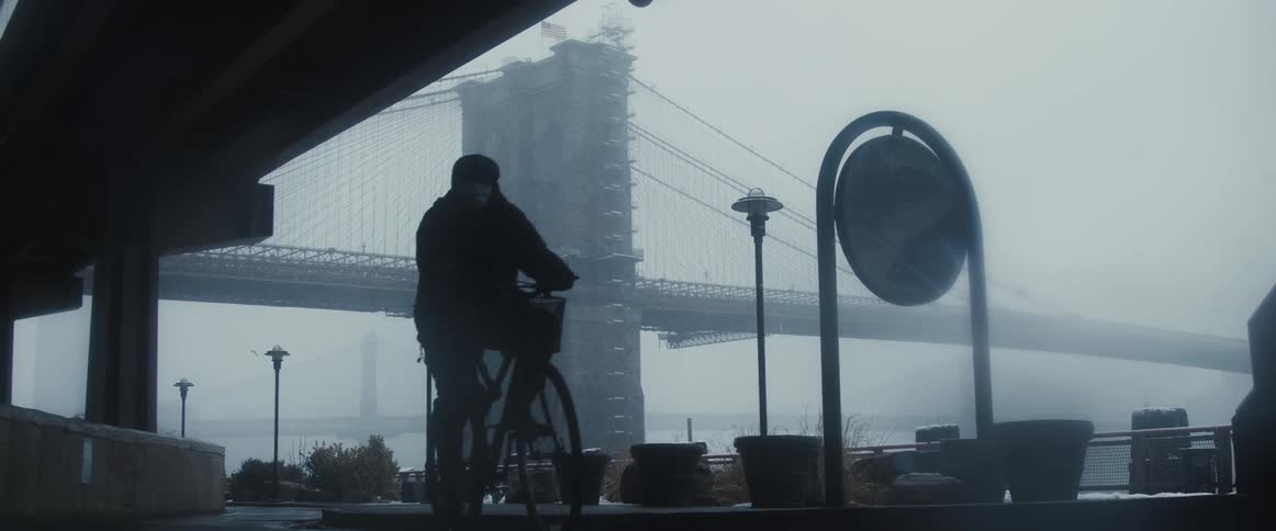 A man bikes down a city sidewalk in the fog