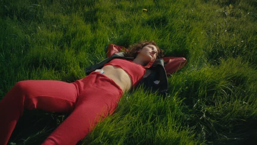 A woman lies in a grassy field with flowers blooming