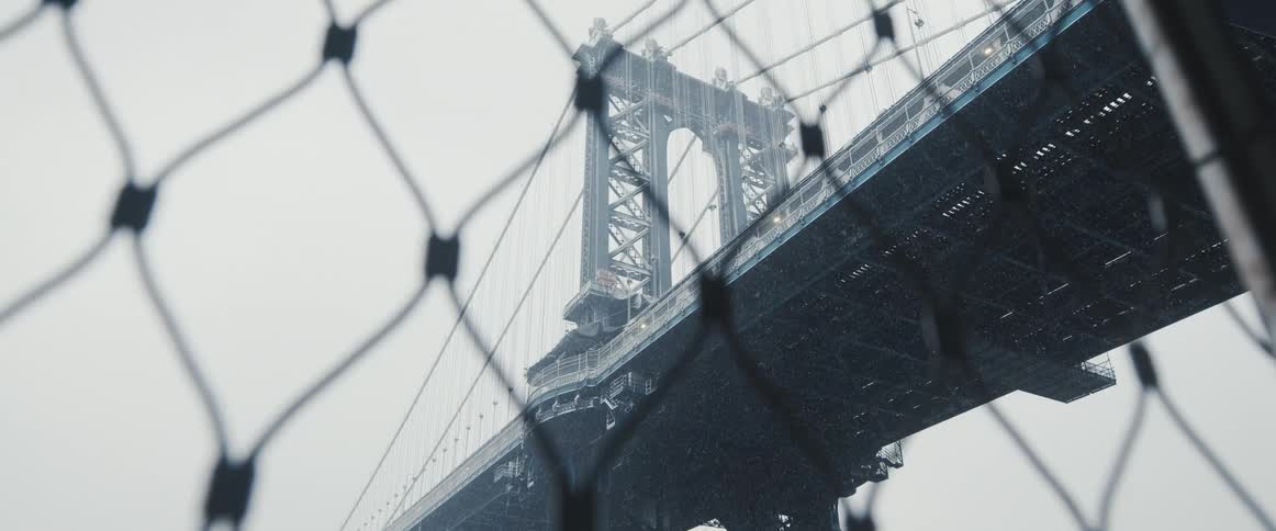 Suspension bridge stands over chain link fence on misty day