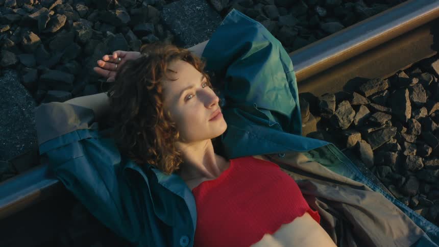 A woman wearing a red halter top and red pants is lying across a train track