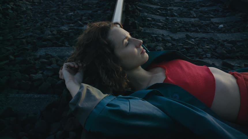 A woman wearing a red halter top and red pants is lying across a train track