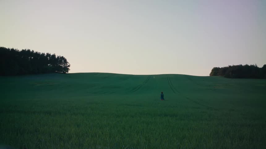 Someone wearing a long dark coat is running in a field of tall grass