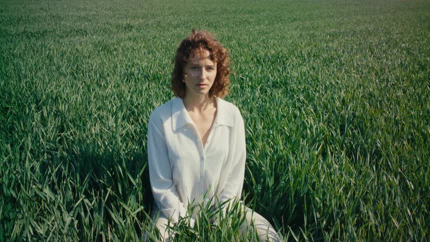 A woman wearing white clothes is sitting an a field of tall grass