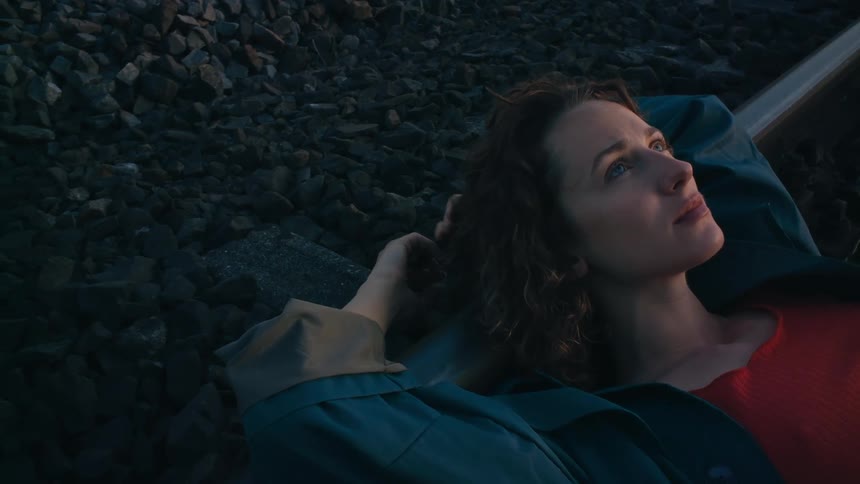 A woman plays with her hair as she lies on train tracks