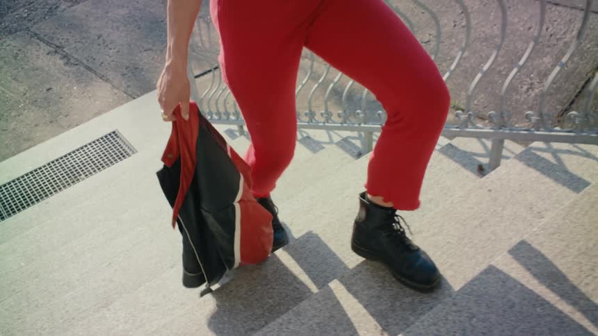 Someone wearing black boots and red pants is walking up stairs carrying a red and black jacket
