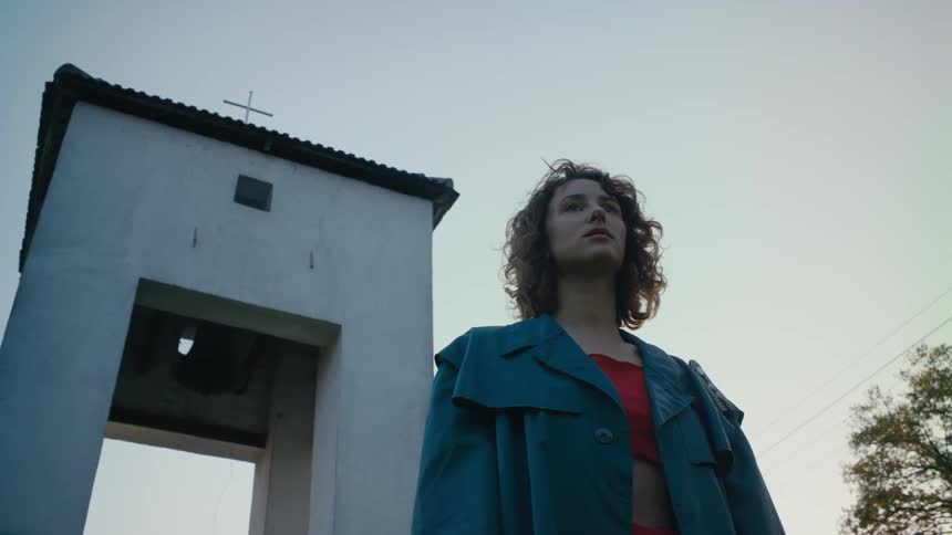 A woman stands in front of a church and looks around