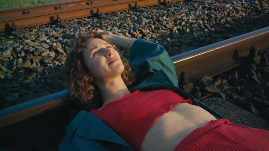 A woman wearing a red halter top and red pants is lying across a train track