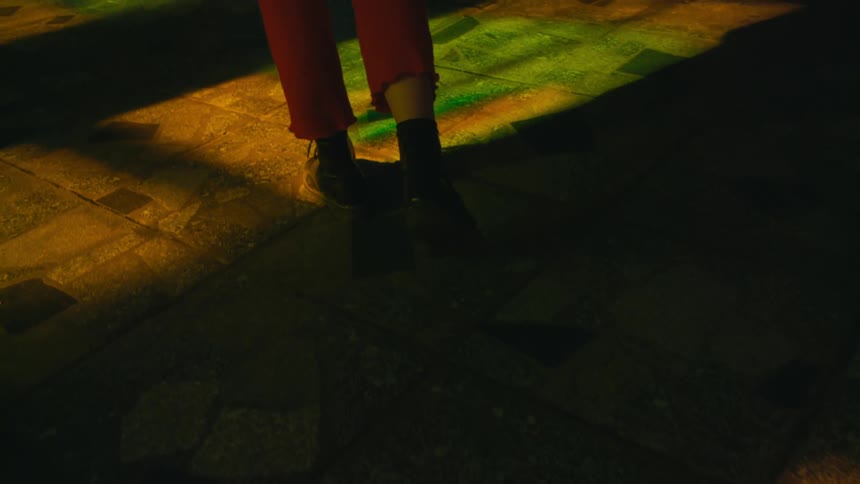The sun shines on painted concrete as someone wearing red pants and black boots is walking on it