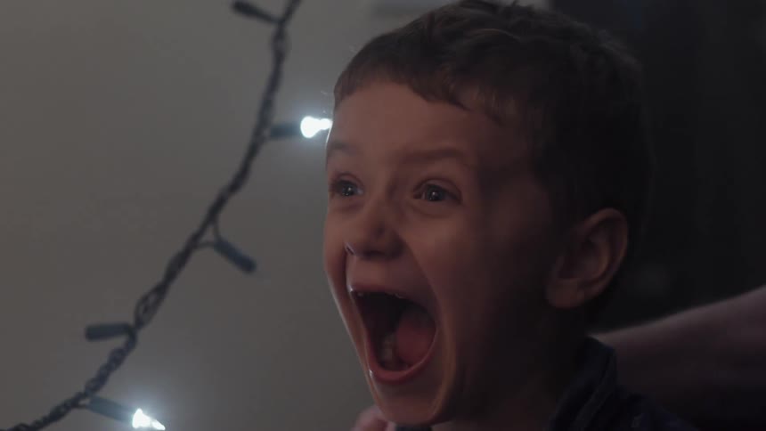 With white christmas lights hanging beside him, a happy boy yells