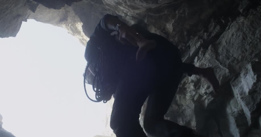 A man carries equipment and a small child out of cave