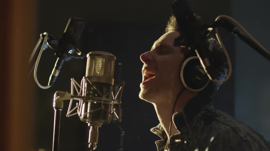A man is singing into a microphone wearing headphones