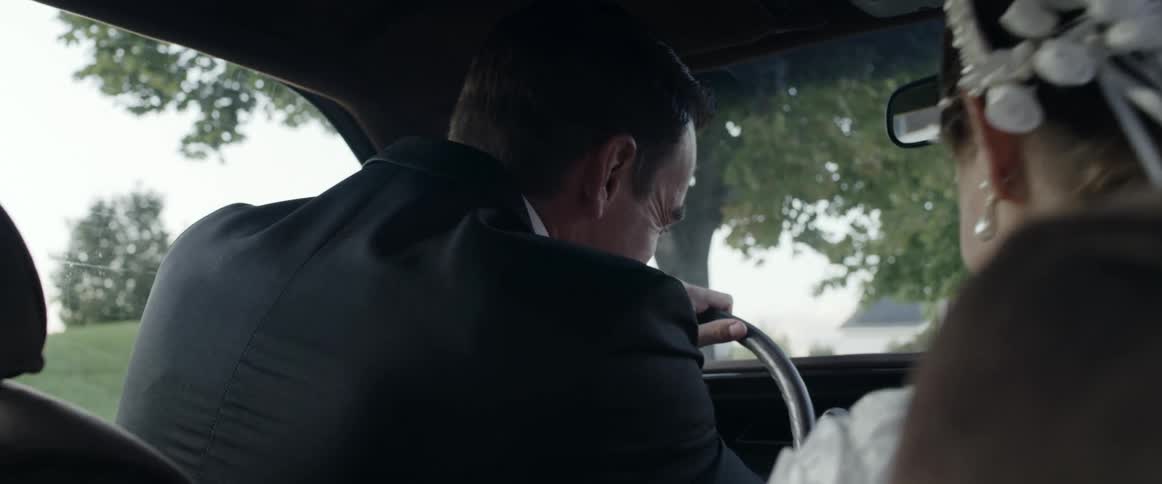A groom smiles at his new bride while starting their car