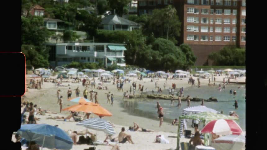 Vintage film of people sitting on the beach and playing in the water