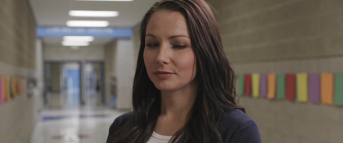 A woman standing in a school corridor turns her head to look into the camera