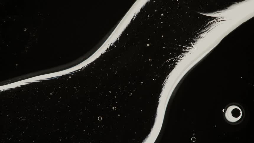 Small white bubbles are incased in a larger liquid like bubble in a dark place
