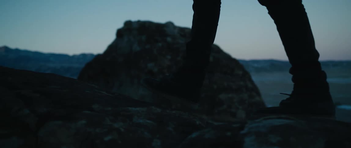 Hiker wearing hiking boots walks over the rocks as mountains sit in the distance