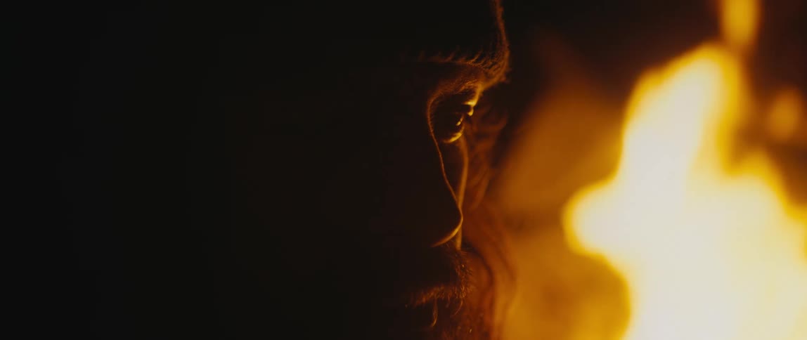 Man with a beard and wearing a hat watches the burning flames