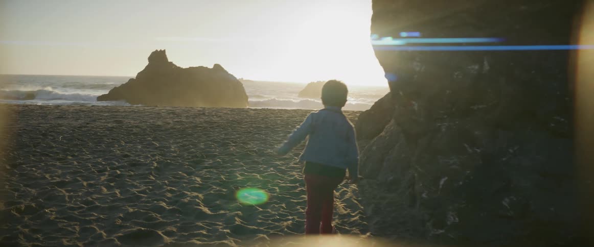 A boy running on the beach sand as waves splash against the rocks near shore