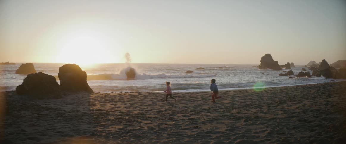 Little boy and girl run on the beach at sunset next to the sea