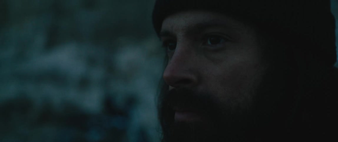 Man with mustache and beard wears a knit hat while standing outdoors amongst snow