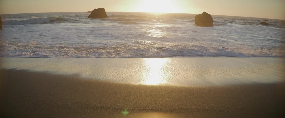 Ocean waves splash and foam on a sandy shore at sunset