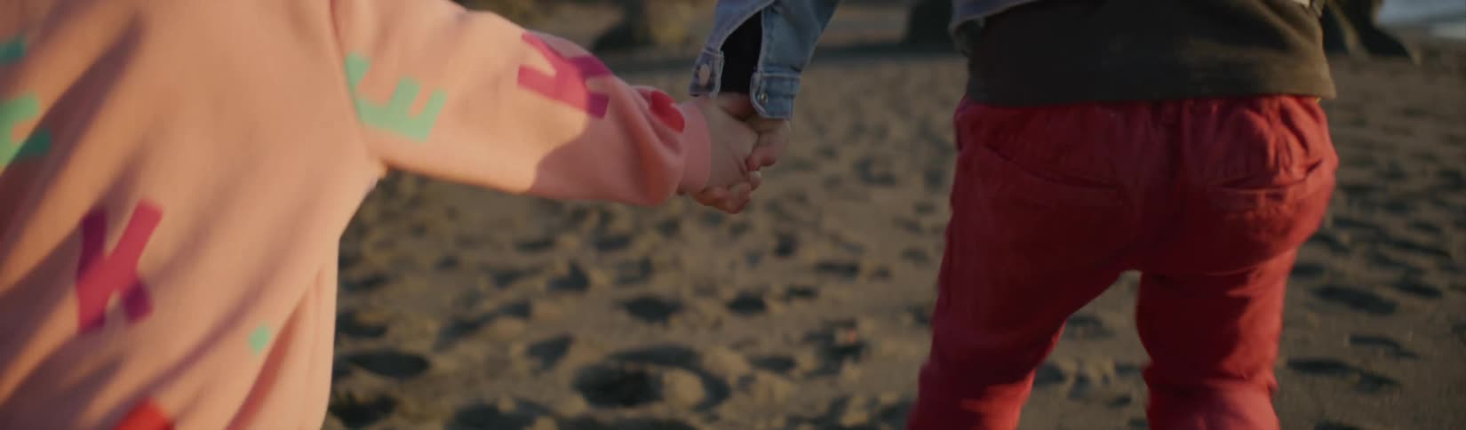 A little boy and girl run on the beach holding hands