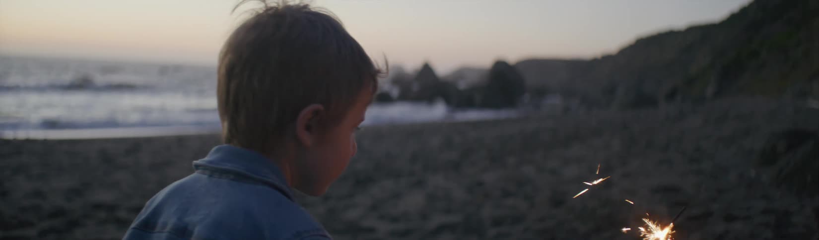 A boy standing on the beach holding a sparkler turns and begins to run