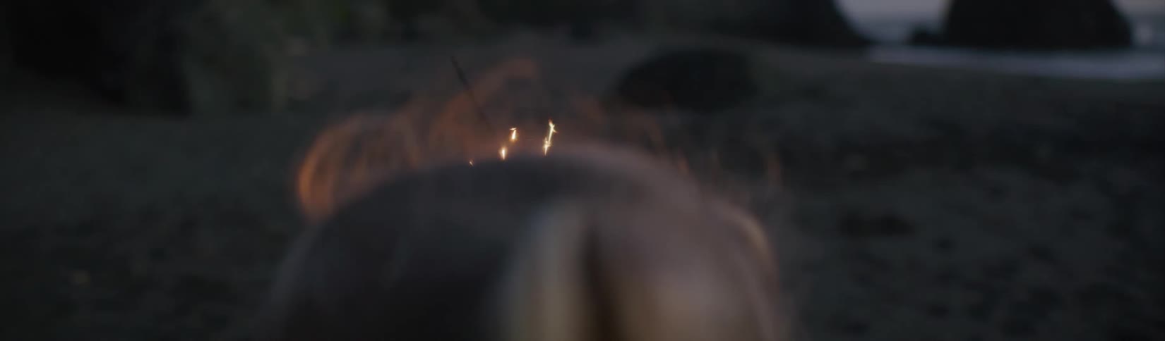 A young girl runs across a beach while holding a sparkler in the evening