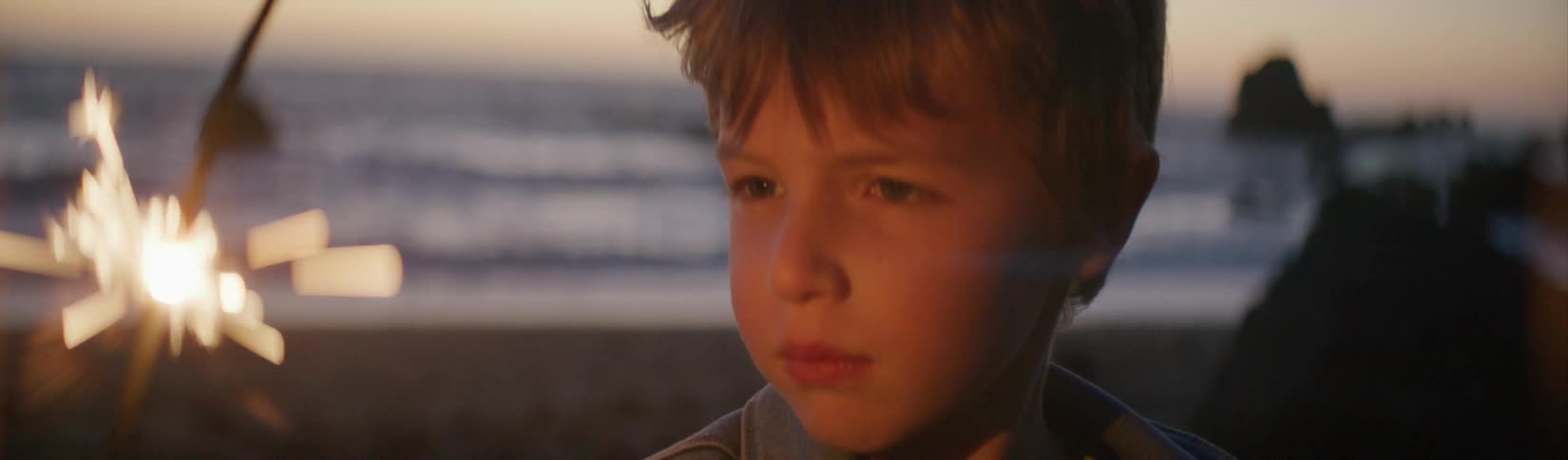 A boy is holding a sparkler on the beach
