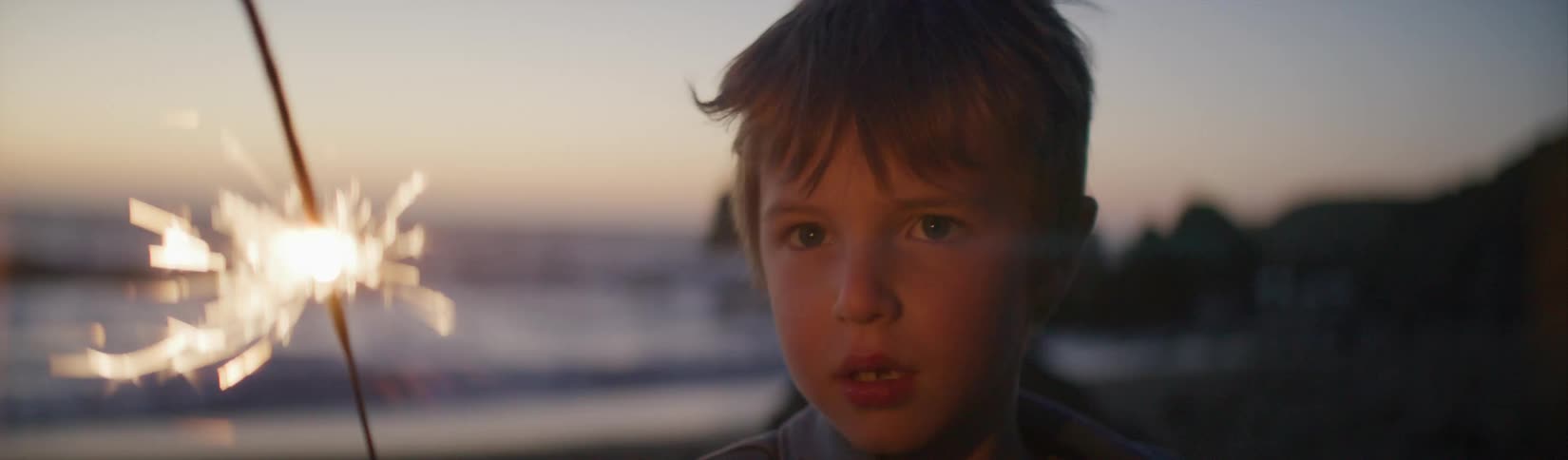 A little boy waves a sparkler around at the beach