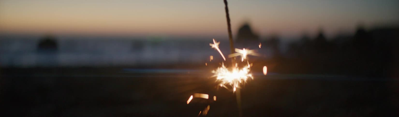 A person holds a sparkler upside down on the beach