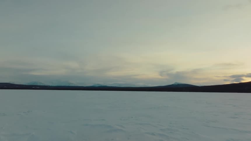A thick blanket of snow covers a flat field near rolling hills