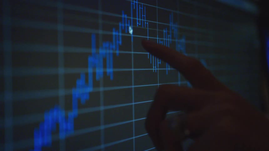 A person is pointing to a chart on the monitor
