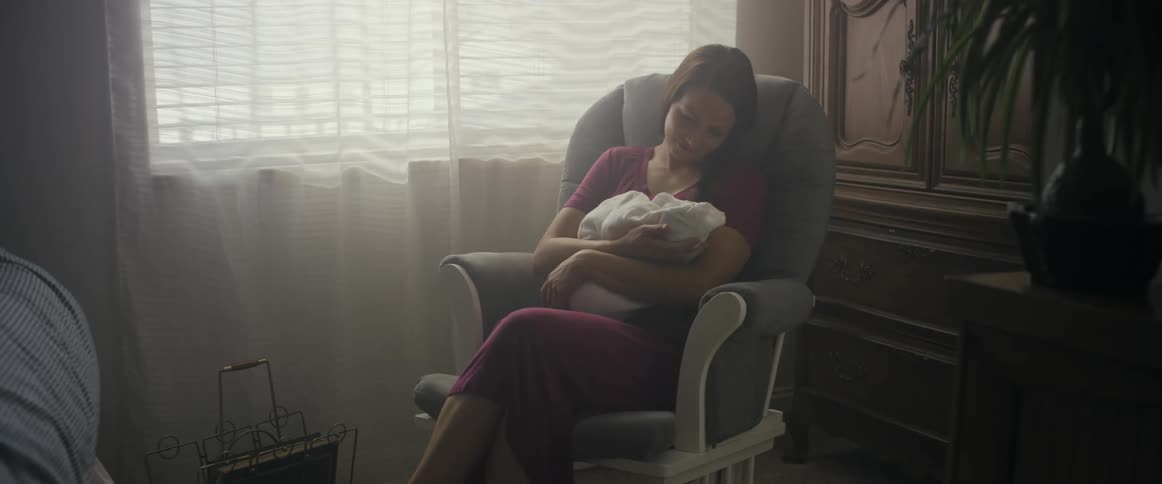 A woman sits at home and rocks her baby