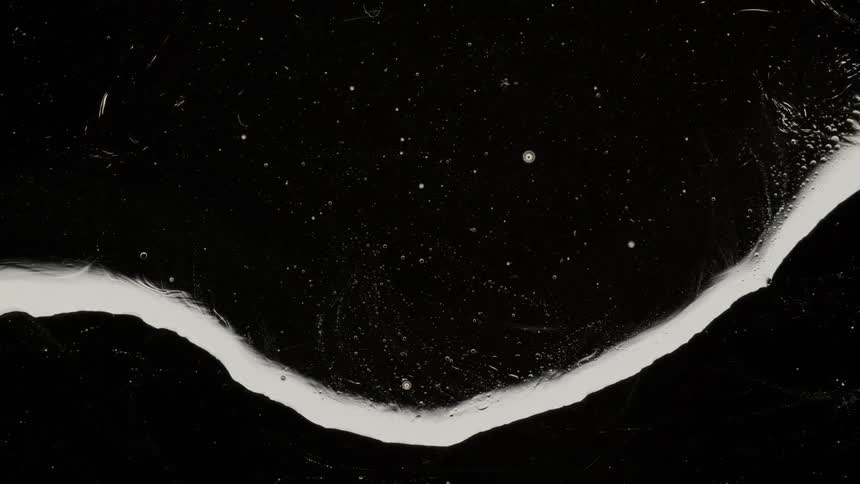 Small white bubbles are incased in a larger liquid like bubble in a dark place