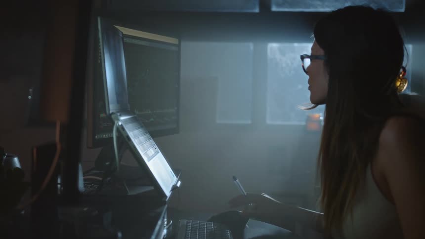 Woman sitting at the desk looking to the laptop and computer screens in front of her and using a plastic calculator