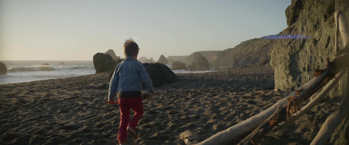 A young boy carrying a rock and stick walks along the beach
