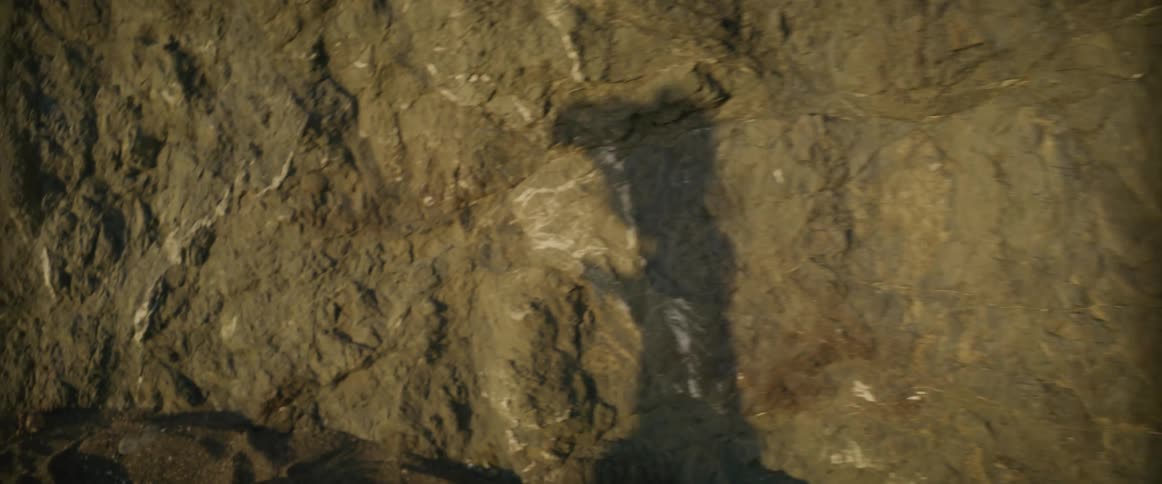 Shadow cast by girl moves across rock as girl walks onto sandy beach