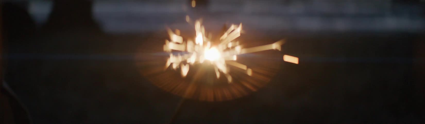 A young boy holding a burning sparkler outside at dusk