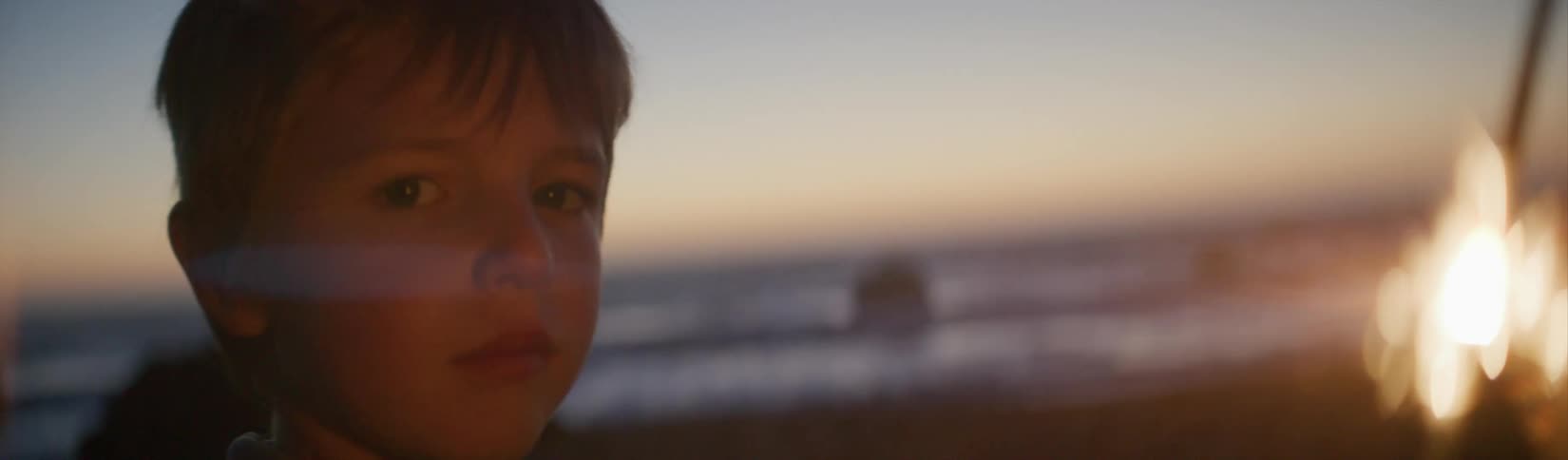 Child holding sparkler on beach at night stares