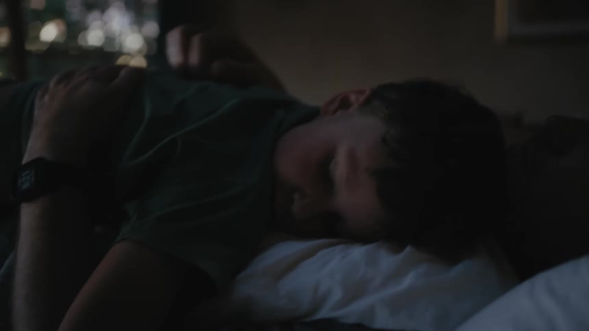 A woman rubs her sons ack while he lies on her chest in bed