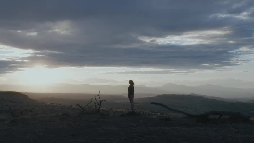 A woman stands in a soiled flat area and looks across the landscape