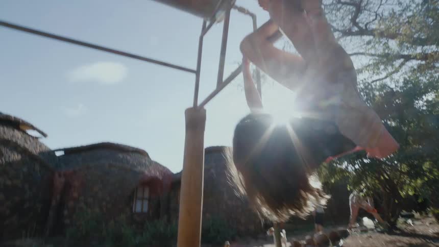 A young girl swings upside down from a makeshift pull up bar in her familys yard
