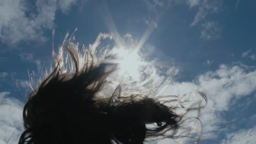 Back of a woman waving her long hair in the wind under the blue sky on a sunny day